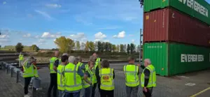 Raadsleden van gemeente Doesburg in CTD-hesjes krijgen uitleg bij gestapelde zeecontainers op Container Terminal Doesburg aan de IJssel.