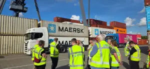Raadsleden van gemeente Doesburg kijken bij Container Terminal Doesburg naar een vrachtwagen met zeecontainers onder de containerkraan.